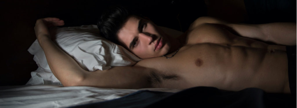 Shirtless man lounging on bed looking at the camera with bedroom eyes